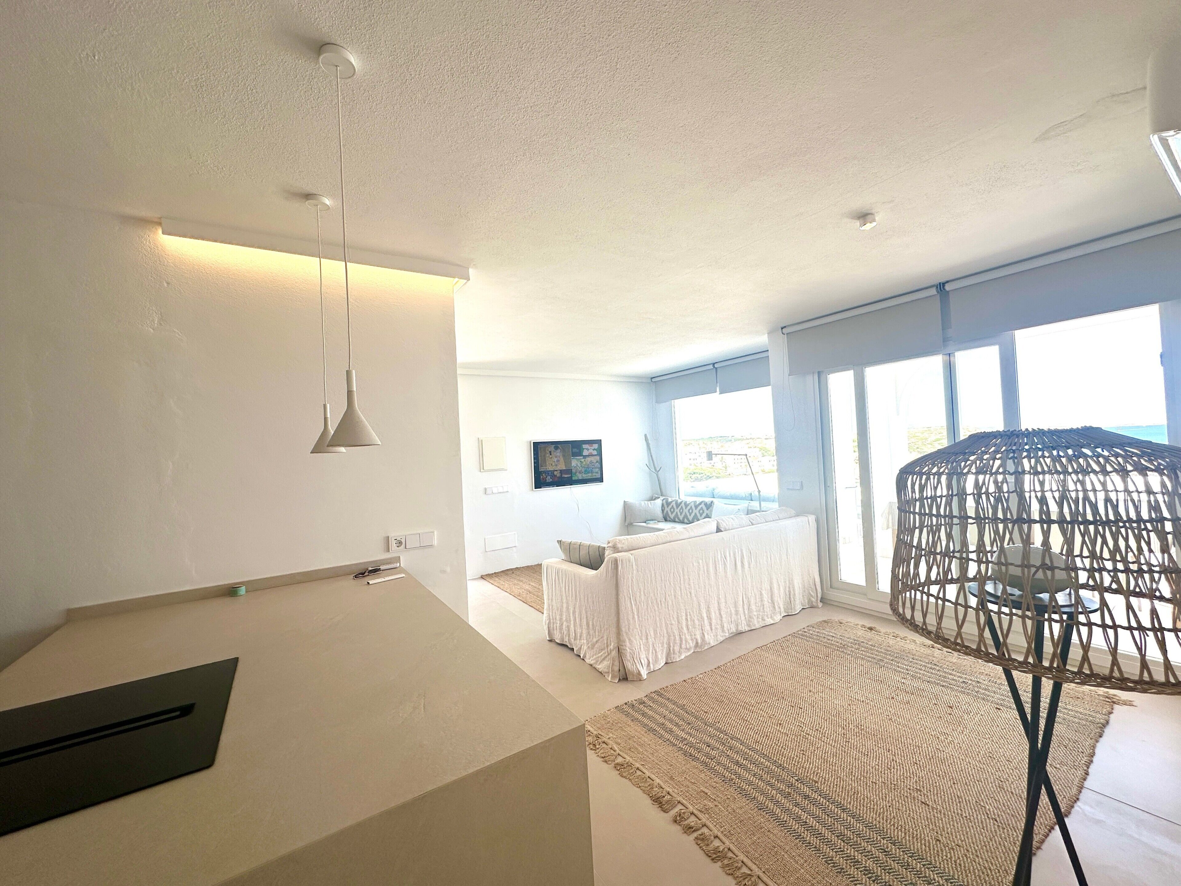 A modern living room with a sofa, a coffee table, a hanging chair, and a large window with a view.