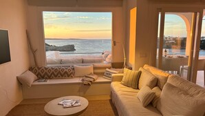 Una sala de estar con un ventanal grande con vista al mar, un sofá, una mesa de centro y una pequeña mesa con una botella y vasos.
