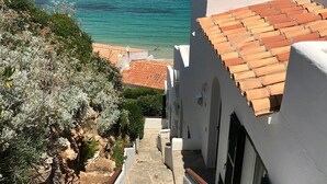 Un edificio costero con una escalera de piedra que baja a la playa, paredes blancas y vista al mar.