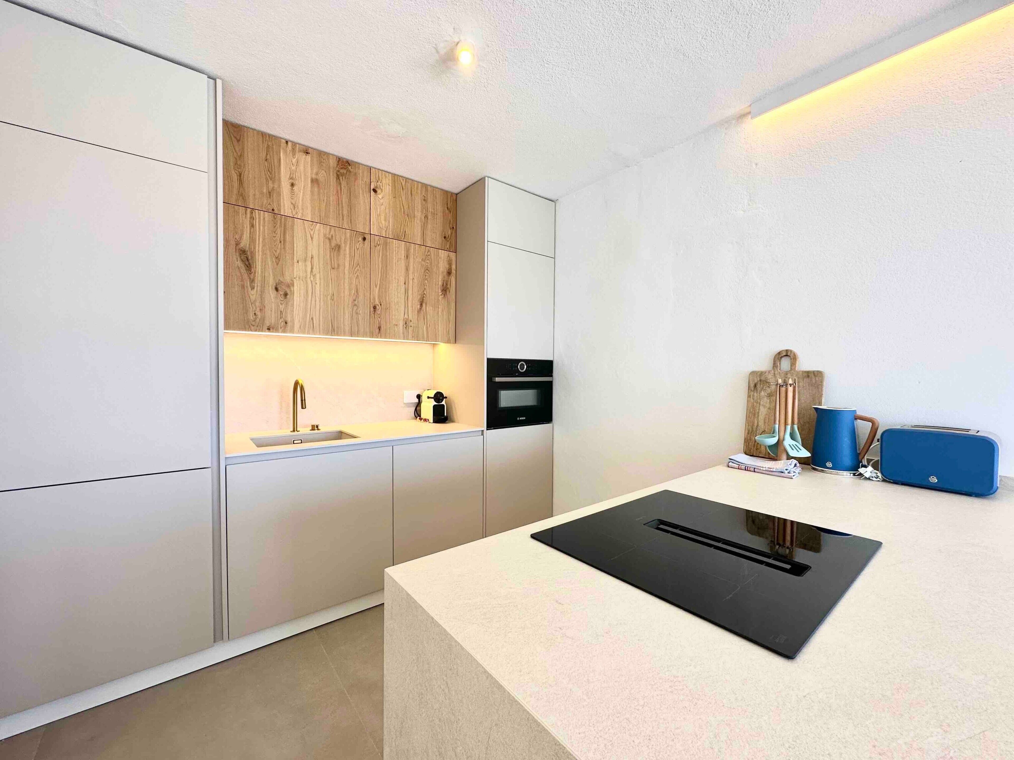 Une cuisine moderne dotée d’un four encastré, d’un évier et d’un plan de travail avec une plaque de cuisson à induction noire.