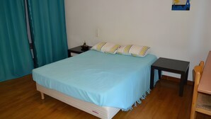 Ein Einzelbett mit hellblau gestepptem Überwurf, ein Nachttisch mit Lampe und ein kleiner Beistelltisch.