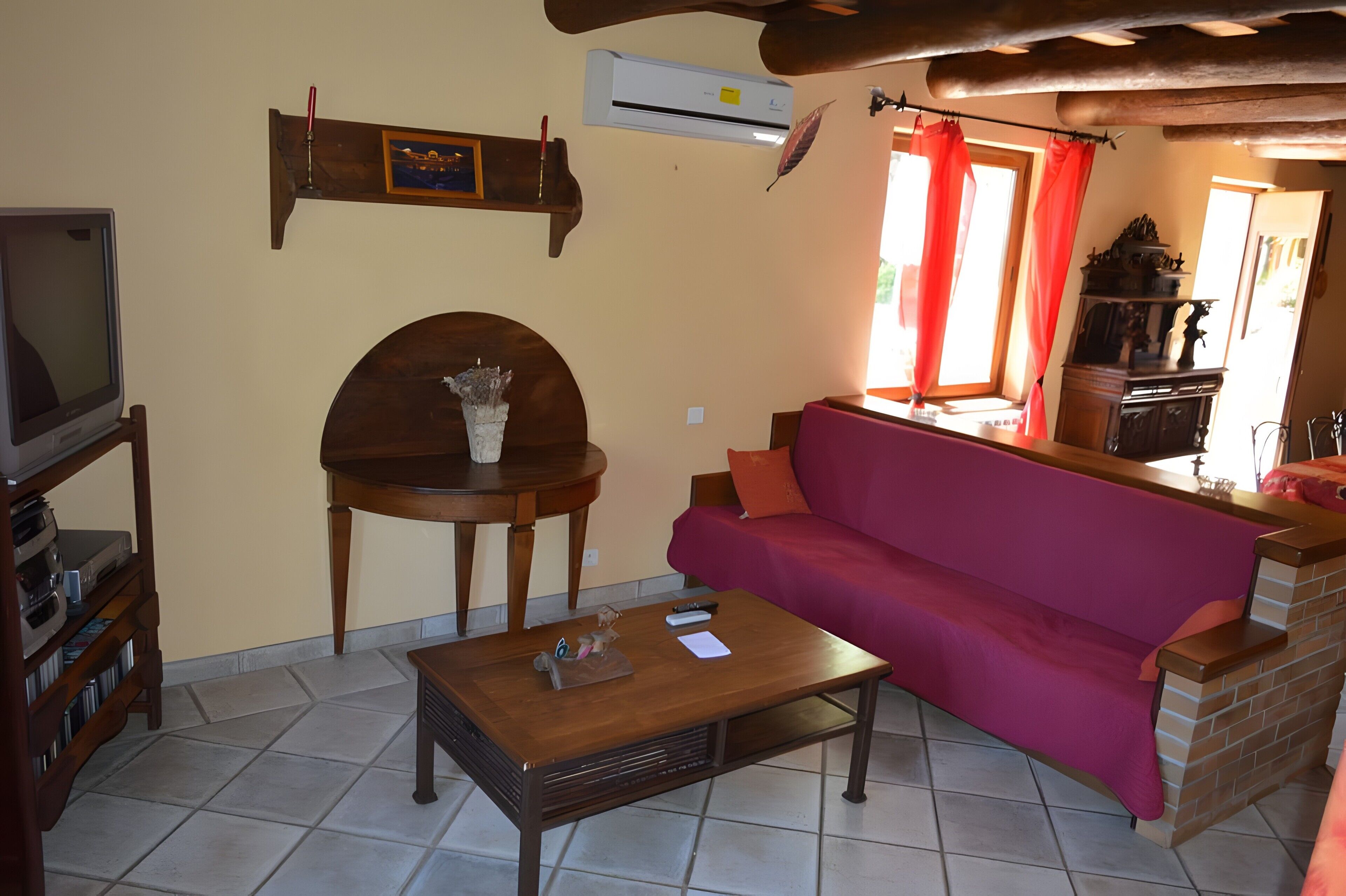 Un salon avec une télévision, une table basse en bois, un canapé rouge et une cheminée.