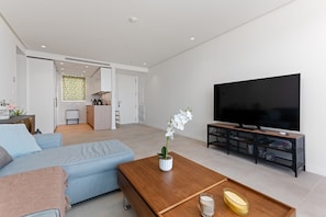 A modern living room with a sofa, coffee table, TV, and a kitchen area in the background.
