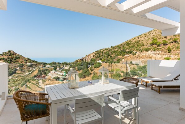 A terrace with a table and chairs, a wicker chair, two lanterns, and lounge chairs with a view of the landscape and sea. - Apartment 'Palo Alto' with Sea View, Wi-Fi and Air Conditioning (Marbella)