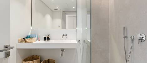 Un baño moderno con cabina de ducha de vidrio, un lavamanos blanco y dos cestos de mimbre.