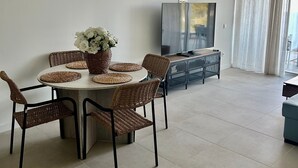 A dining area with a round table, wicker chairs, a vase with flowers, a flat-screen TV, and a sliding glass door.