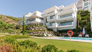 A modern multi-story hotel with a swimming pool, lush greenery, and a rocky hillside backdrop.