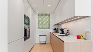 A modern kitchen with white cabinets, a countertop, a sink, and a trash bin.