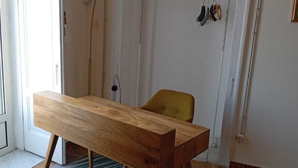 Ein Zimmer mit einem Holztisch, einem gelben Stuhl, einer Stehlampe und einem gemusterten Teppich.