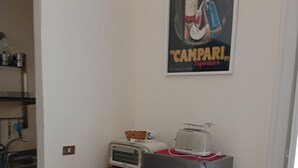 Et lille køkken med et køleskab, en brødrister og et lille bord. En plakat er hængt på væggen over disken.