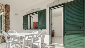 Ein weißer Tisch mit Stühlen, eine Steinsäule und grüne Fensterläden an Türen.