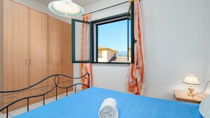 Ein Schlafzimmer mit einem Bett, einem Fenster mit Vorhängen, einem Nachttisch mit Lampe und Holzmöbeln.