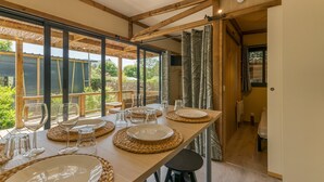Een eetgedeelte met een lange tafel, helder servies, geweven placemats en uitzicht op groen buiten.