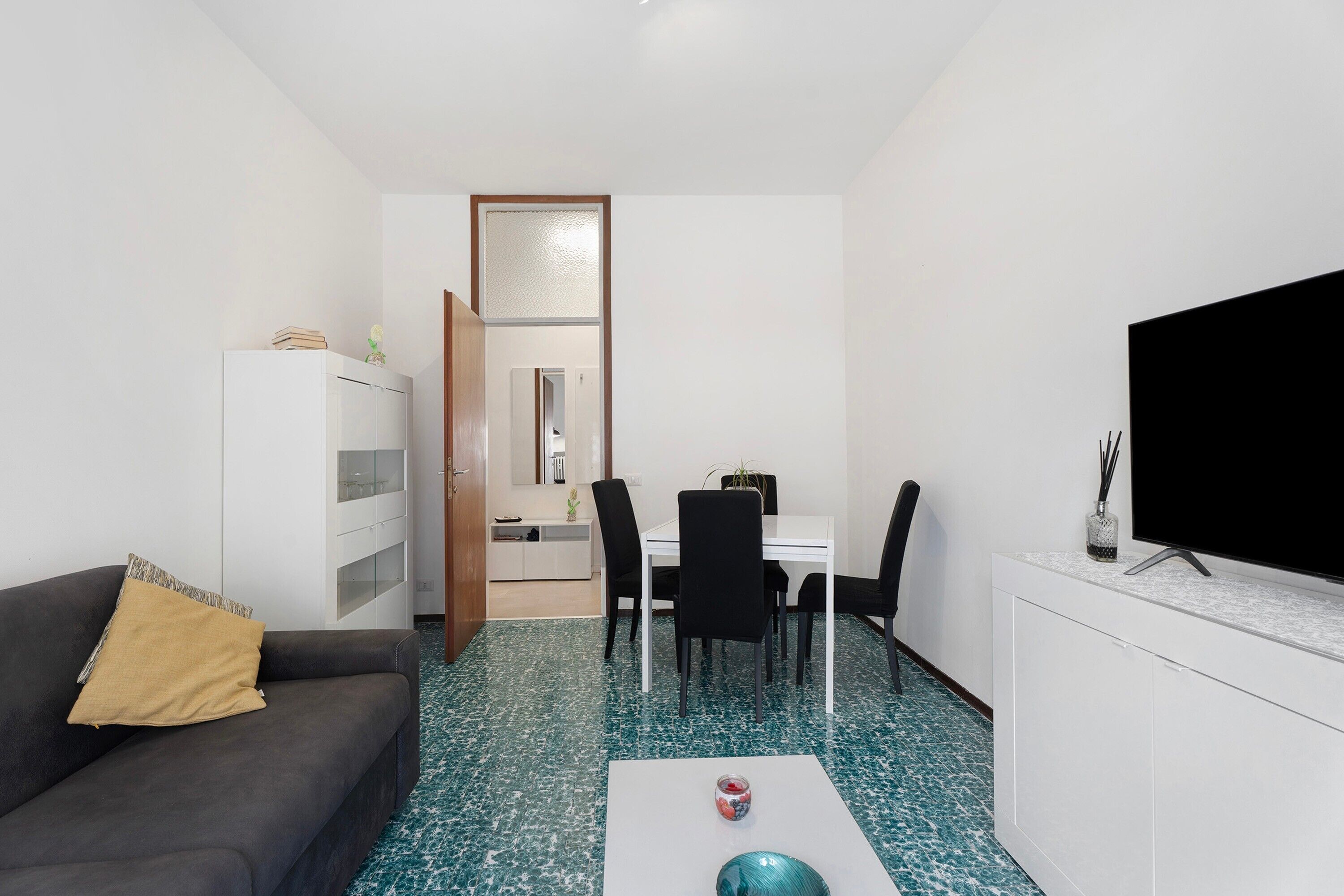 Ein kompakter Wohnbereich mit Sofa, Esstisch mit Stühlen, Fernseher und Schrank.