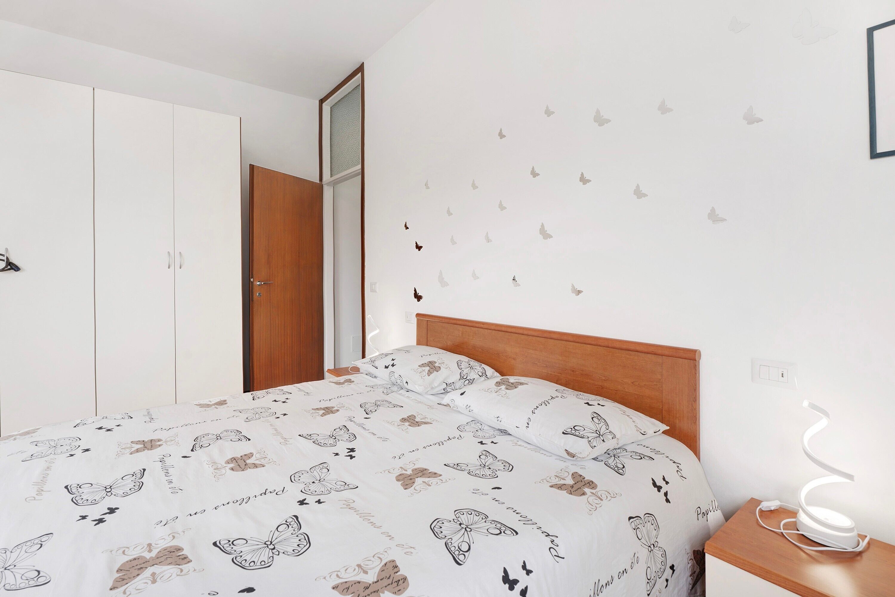 Una camera da letto con un letto, un armadio, un comodino con una lampada e decorazioni murali a forma di farfalla.