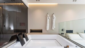 Une salle de bain moderne avec une grande baignoire, une douche en verre et un lit recouvert de linge de maison blanc.