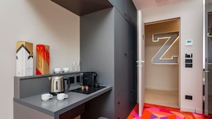 Une chambre d’hôtel compacte comprenant un coin cuisine, un lit, une armoire et une porte marquée d’un grand « Z ».