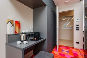 Ein kleines Hotelzimmer mit Küchenzeile, einem Bett, einem Kleiderschrank und einer Tür, die mit einem großen 'Z' gekennzeichnet ist.