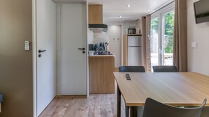Eine kompakte Küche mit Mikrowelle, Herd und einer kleinen Arbeitsfläche. Ein Esstisch mit Stühlen und ein an der Wand befestigter Fernseher sind vorhanden.