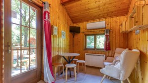 Interior de una cabaña de madera con una mesa de comedor, cuatro taburetes, un sofá, un televisor y un equipo de aire acondicionado.