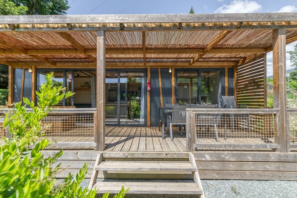 Een houten terras met een overdekte zithoek, een brandblusser en uitzicht op het omliggende landschap.