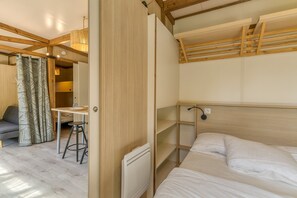 Een kleine kamer met een stapelbed, een bureau met een stoel, een radiator en een kamerkleed met een patroon.