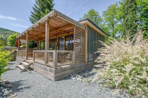 Een houten chalet met een overdekte veranda, grote ramen en een oprit van grind.