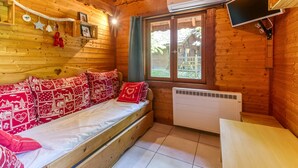 A cozy wooden cabin room with a bed, a window, an air conditioning unit, and a television. - Apartment 'Narcisse' with Mountain View, Wi-Fi and Air Conditioning (Vaulnaveys-le-Bas)