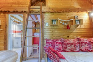 A wooden cabin interior with a bed, a ladder, a shelf with framed pictures, and a bathroom visible through a glass door. - Apartment 'Narcisse' with Mountain View, Wi-Fi and Air Conditioning (Vaulnaveys-le-Bas)