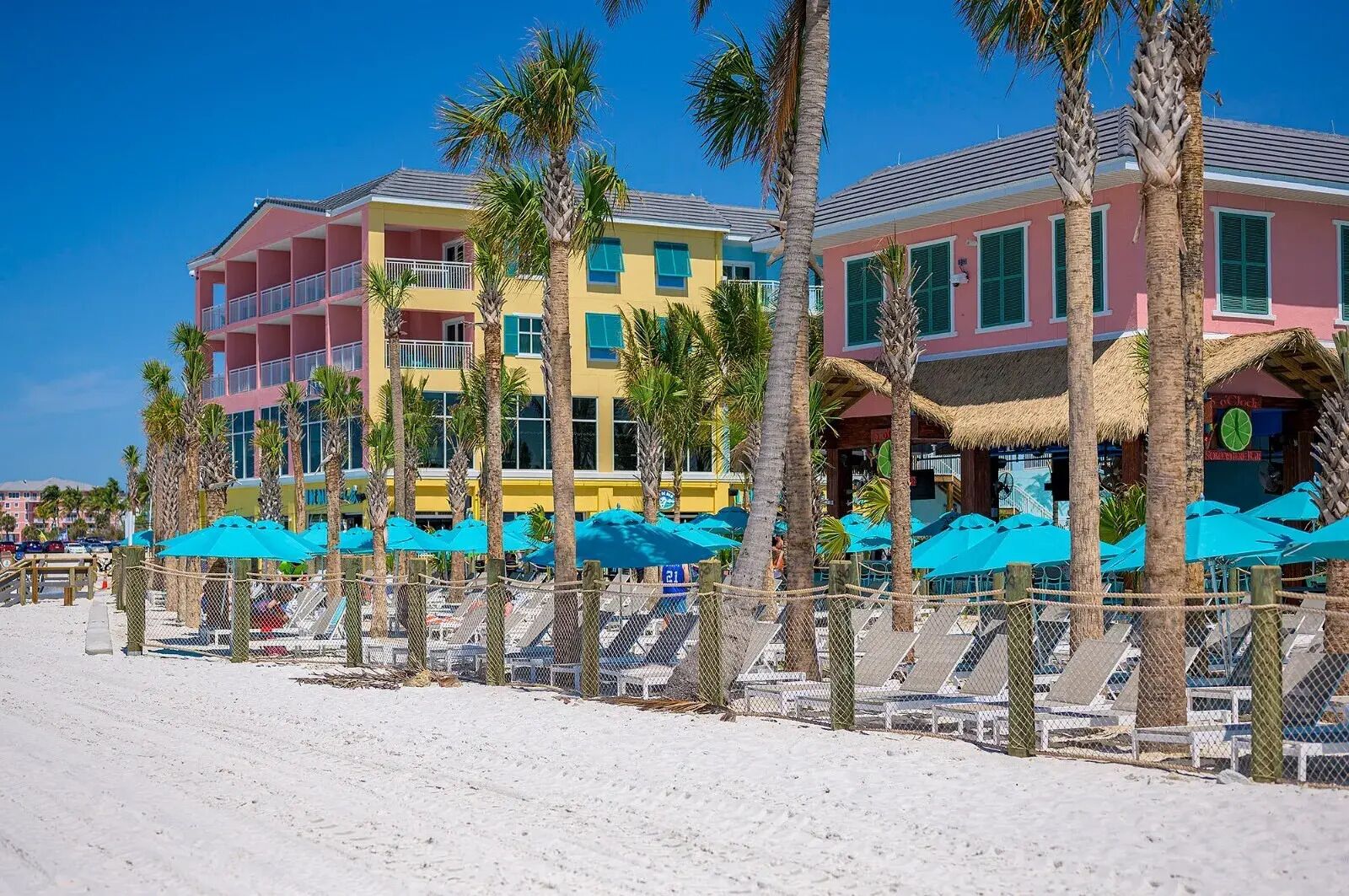 A beachfront hotel with multiple colorful buildings, palm trees, and beach umbrellas.
