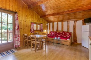 Interior de una cabaña de madera con una mesa de comedor, sillas, un sofá y un refrigerador.