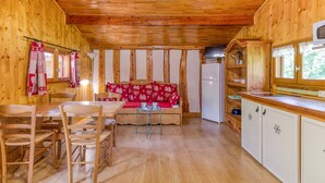 Interieur van een houten chalet met een eethoek, een bank met kussens met hartjesprint, een koelkast en houten kasten.