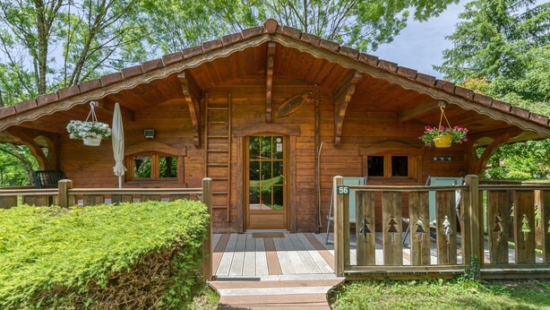 Een houten vakantiehuisje met een veranda, een deur en een bord met het nummer 56.