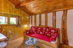 Interior de una cabaña de madera con sofá, mesa de comedor, sillas y una mesita con una revista.