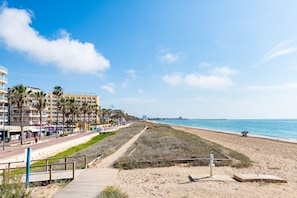 A beachside promenade with a boardwalk, palm trees, and a building with balconies.