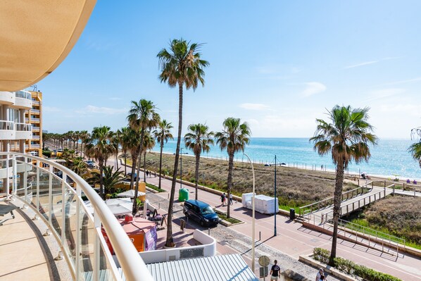 A balcony with a view of a beach, palm trees, and a clear sky.