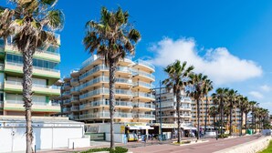 Un hôtel situé en bord de mer, doté de nombreux balcons, de palmiers et offrant une vue sur un ciel dégagé.