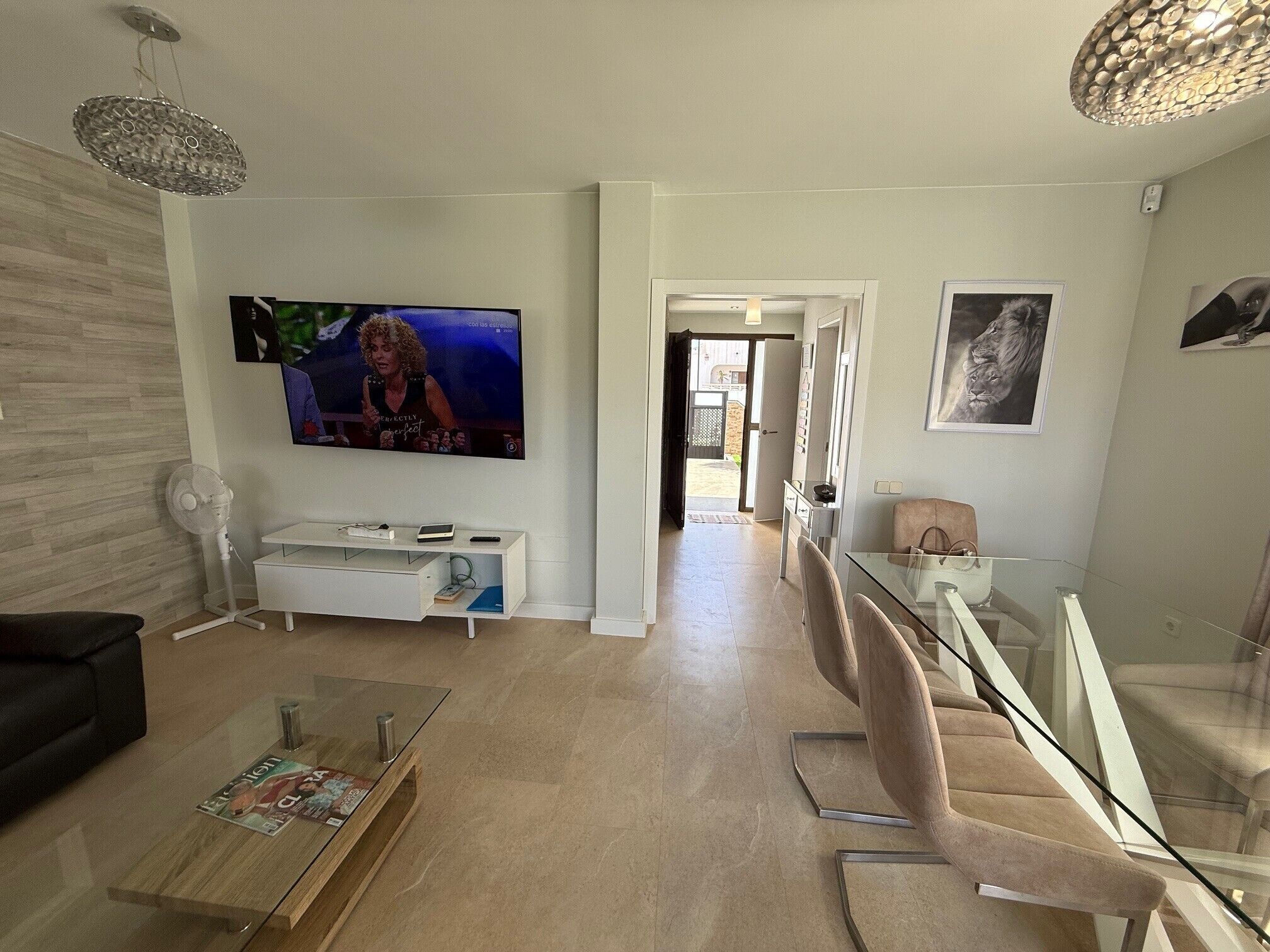 A modern living room with a flat-screen TV, a glass coffee table, a white entertainment unit, and a staircase leading to another level.