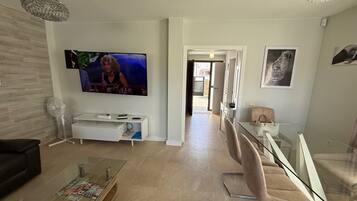 A modern living room with a flat-screen TV, a glass coffee table, a white entertainment unit, and a staircase leading to another level.