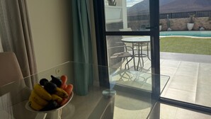 A room with a glass door leading to an outdoor patio with a pool, chairs, and a cactus.
