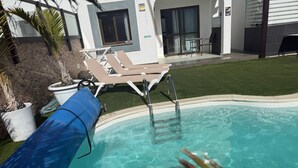 A swimming pool with lounge chairs, a covered area, and a building with a sign.