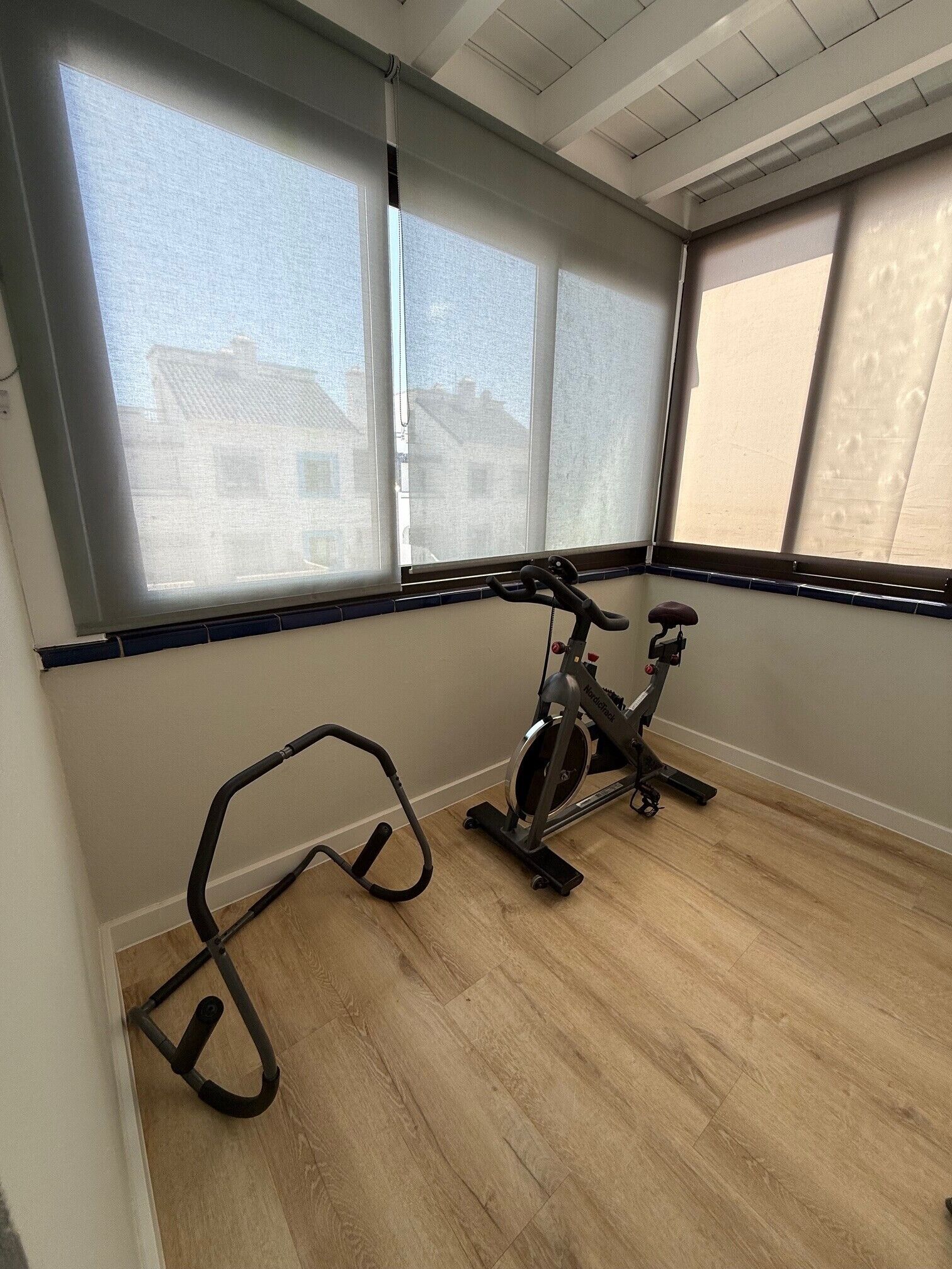 A room with a stationary bike, large windows with blinds, and a wooden floor.