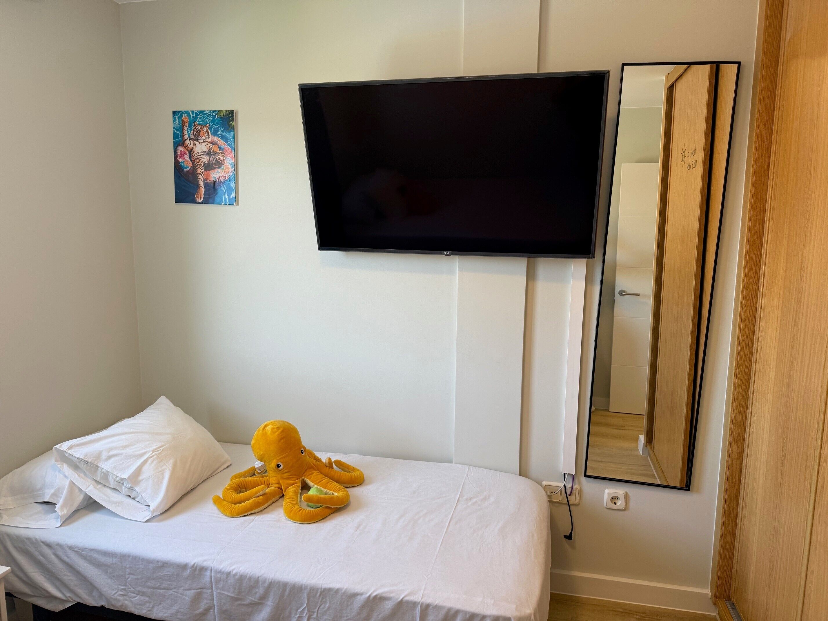 A bedroom with a bed, a TV mounted on the wall, a mirror, and a painting.