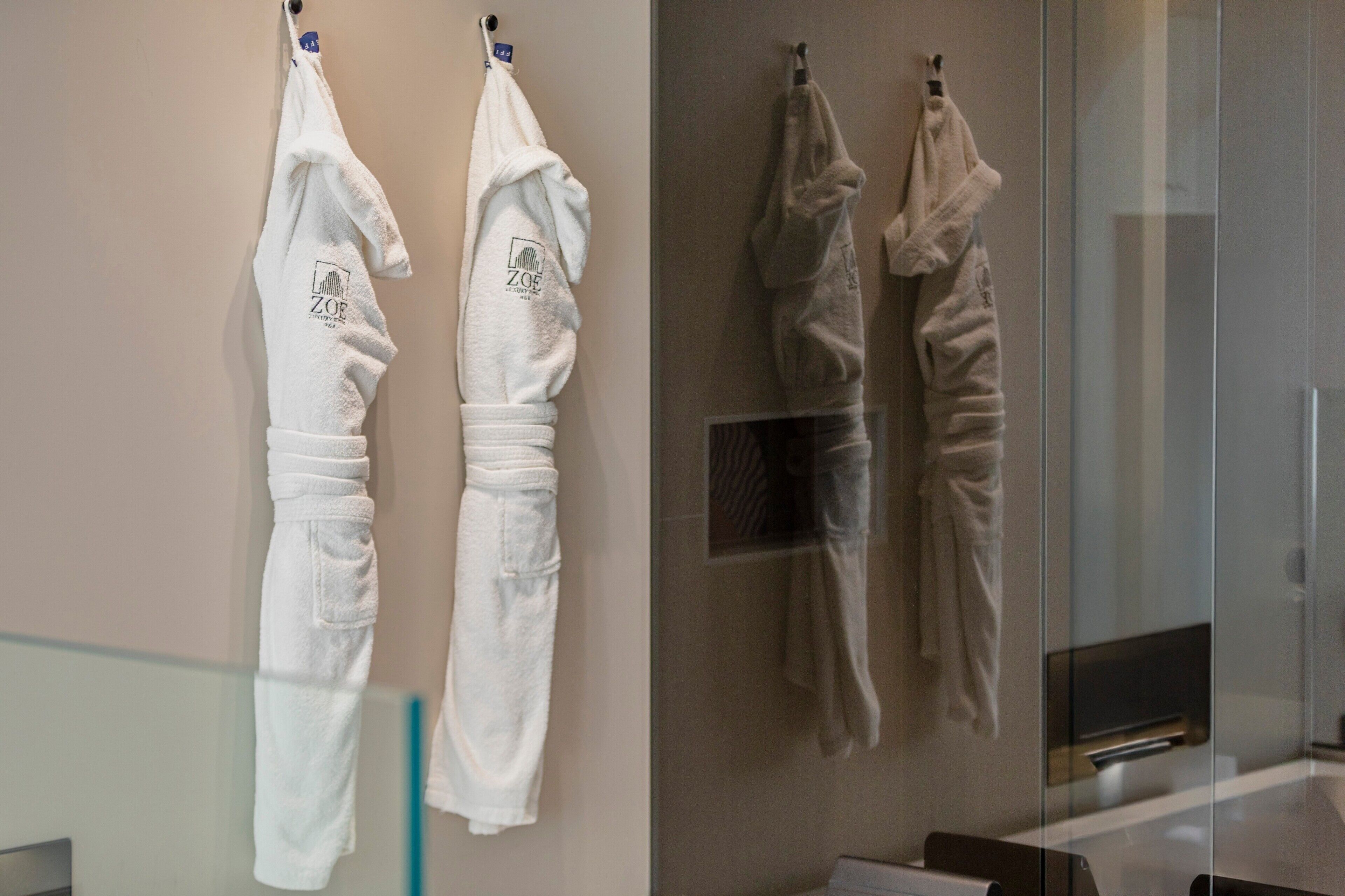 A bathroom with two white robes hanging on hooks, a glass shower enclosure, and a visible sink.