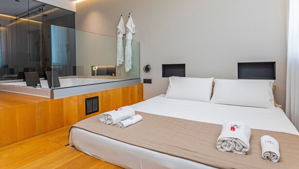 A modern hotel room with a large bed, a wooden headboard, a glass shower enclosure, and a large mirror. - Bed and Breakfast 'Zoe Luxury Suites - Deluxe 03' with Sea View, Wi-Fi and Air Conditioning (Catania)