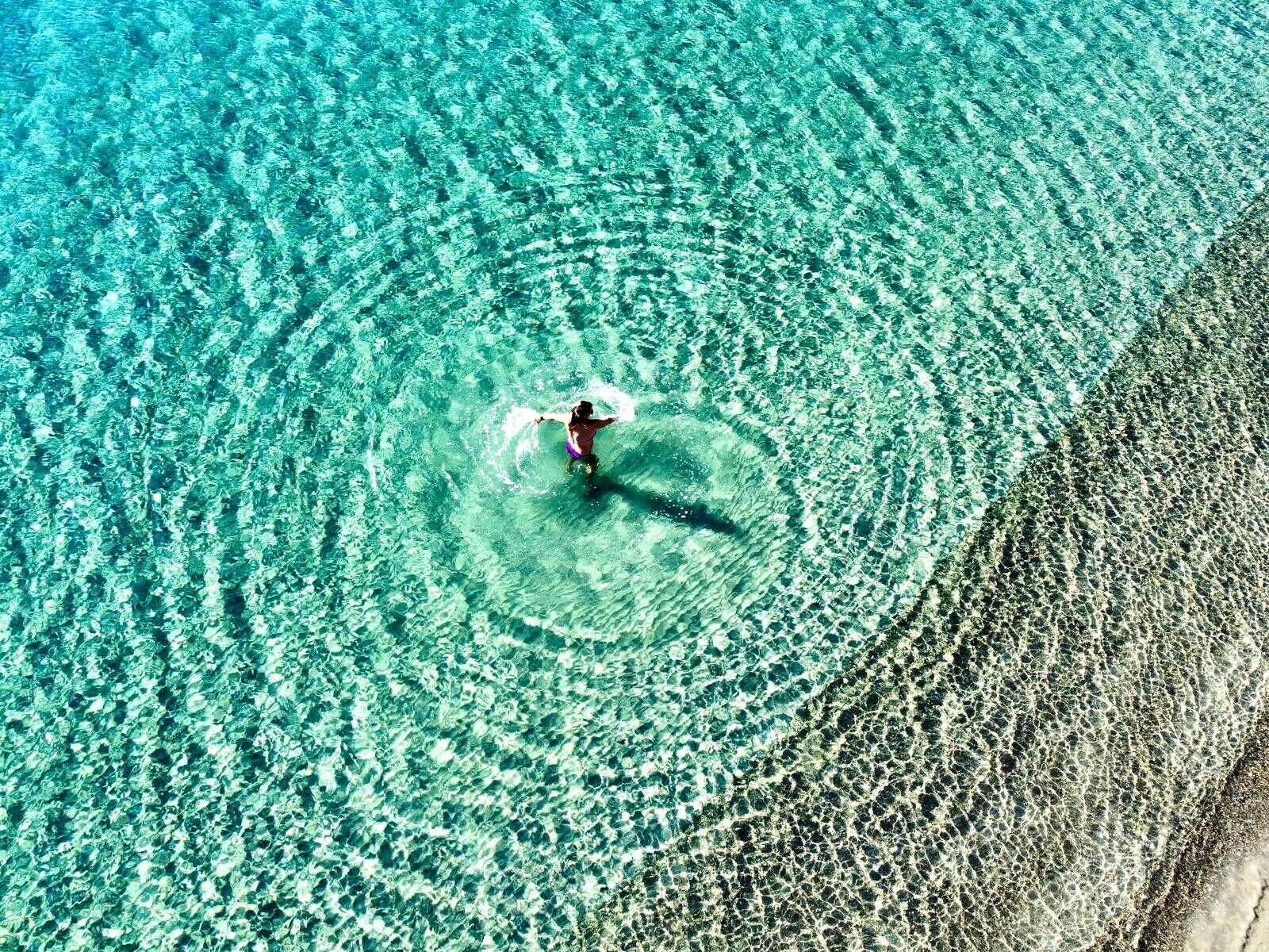Una persona che fa surf su una spiaggia cristallina color turchese.