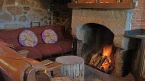 Un mur de pierres, une cheminée avec un feu de bois, un canapé rouge et une chaise en bois.