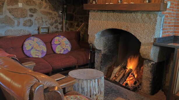 Un mur de pierres, une cheminée avec un feu de bois, un canapé rouge et une chaise en bois.