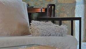 Un salon comprenant un canapé, un coussin moelleux, une table basse en verre et une table d’appoint en bois sur laquelle se trouvent une télécommande et une boîte.
