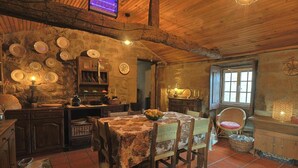 Une cuisine rustique avec des murs en pierre, des poutres en bois et un coin repas comprenant une table et des chaises.